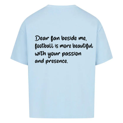 Football Oversized Shirt: Hellblaues Oversized-T-Shirt mit schwarzem Rückendruck: „Dear fan beside me, football is more beautiful with your passion and presence.“